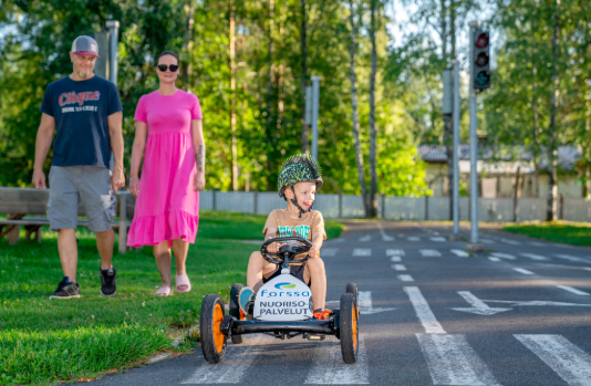 Pieni lapsi polkuautoilemassa lasten liikennepuistossa kesäpäivänä.