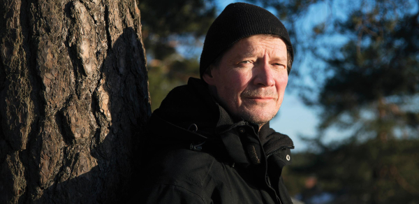 Kirjailija Juha Hurme nojaamassa puuta vasten.