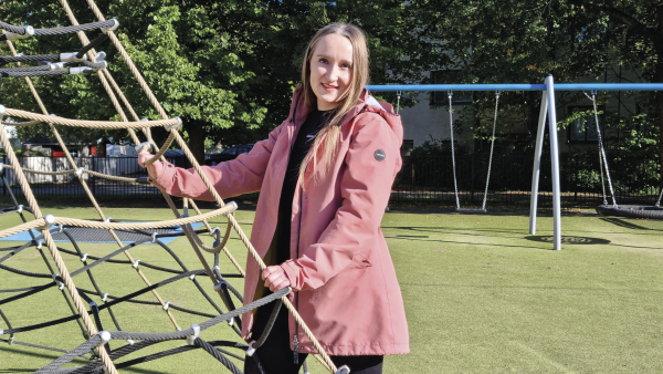 Nainen nojaamassa kiipeilytelineeseen, taustalla keinuja.