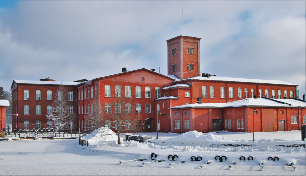 Talvinen maisema, jossa punatiilinen kehräämörakennus lumisena talvipäivänä.