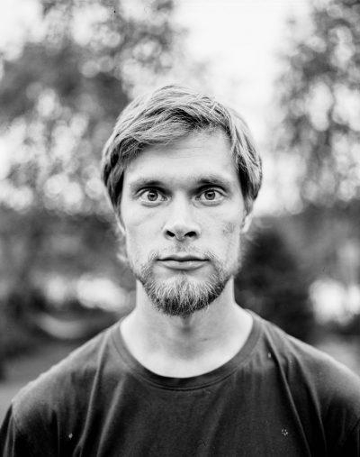 Mustavalkoinen valokuva vakavailmeisestä miehestä katsomassa suoraan kameraan.