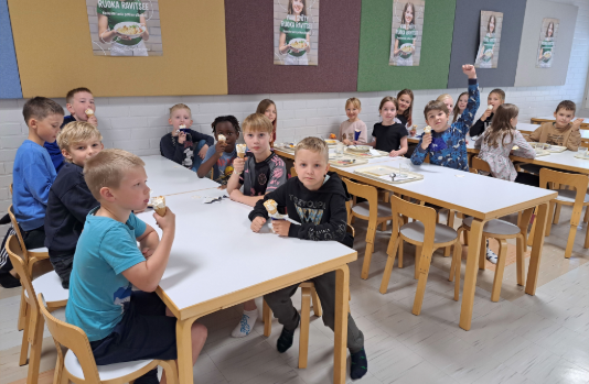 Talsoilan koulun kolmosluokkalaisia syömässä jäätelöä koulun ruokalassa.